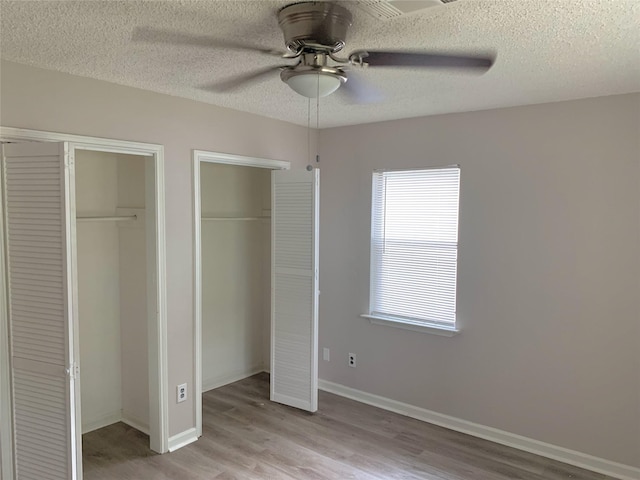 unfurnished bedroom with baseboards, a ceiling fan, wood finished floors, a textured ceiling, and multiple closets