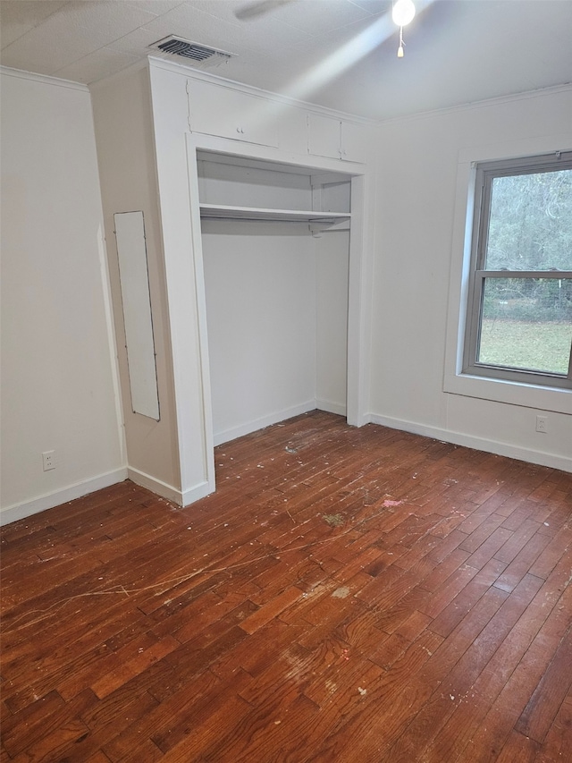 unfurnished bedroom featuring baseboards, visible vents, hardwood / wood-style floors, crown molding, and a closet