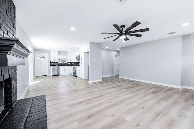 unfurnished living room with ceiling fan, visible vents, baseboards, a brick fireplace, and light wood finished floors