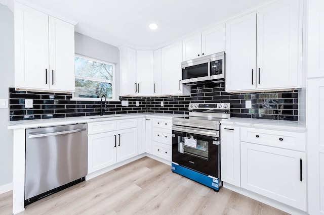 kitchen with a sink, white cabinetry, light wood-style floors, appliances with stainless steel finishes, and decorative backsplash