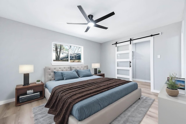 bedroom featuring light wood-style floors, a ceiling fan, baseboards, and a barn door