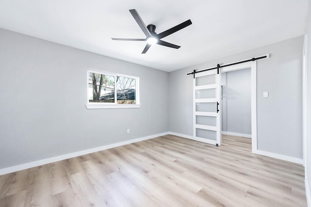 unfurnished bedroom featuring light wood-type flooring, ceiling fan, baseboards, and a barn door