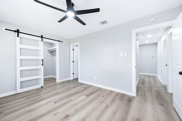 unfurnished bedroom with light wood-style floors, a barn door, visible vents, and attic access