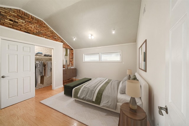 bedroom featuring brick wall, wood finished floors, a spacious closet, vaulted ceiling, and a closet