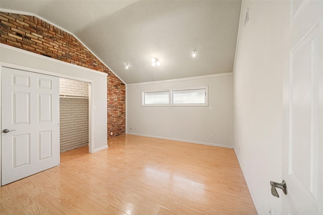 unfurnished bedroom with vaulted ceiling, brick wall, light wood-style flooring, and baseboards