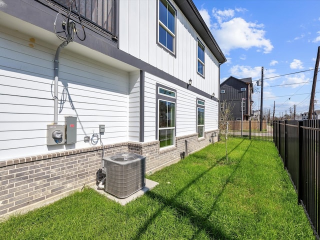 view of property exterior with brick siding, a lawn, a fenced backyard, and central AC unit