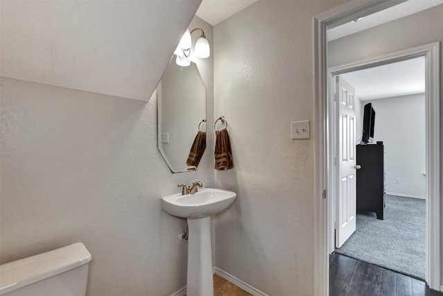 half bathroom with a textured wall, wood finished floors, toilet, and baseboards