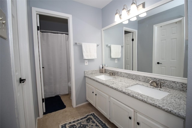 bathroom featuring baseboards, a sink, toilet, and double vanity