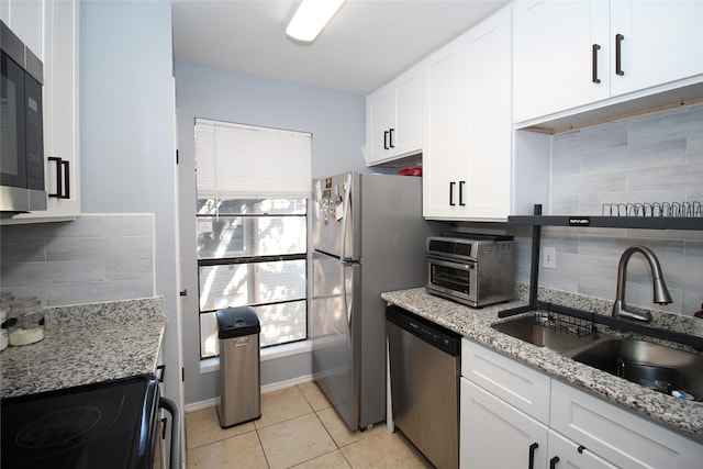 kitchen with decorative backsplash, stainless steel appliances, white cabinetry, a sink, and light tile patterned flooring