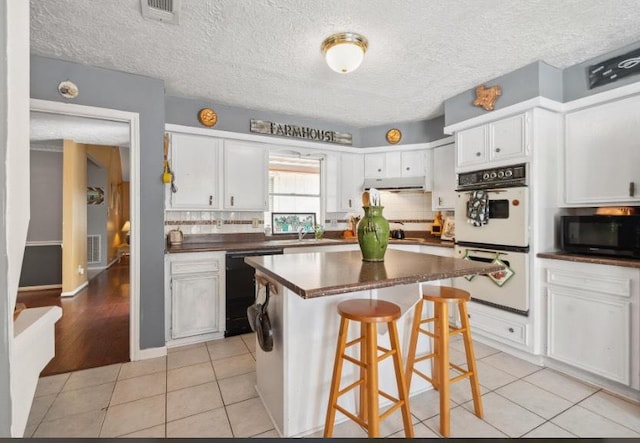 kitchen with under cabinet range hood, dark countertops, double oven, light tile patterned flooring, and dishwasher