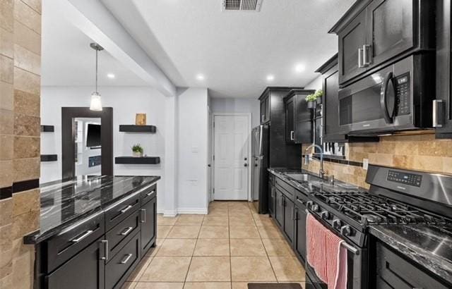 kitchen with dark cabinets, stainless steel appliances, visible vents, decorative backsplash, and dark stone countertops