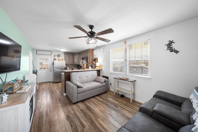 living area with a wall unit AC, ceiling fan, baseboards, and wood finished floors