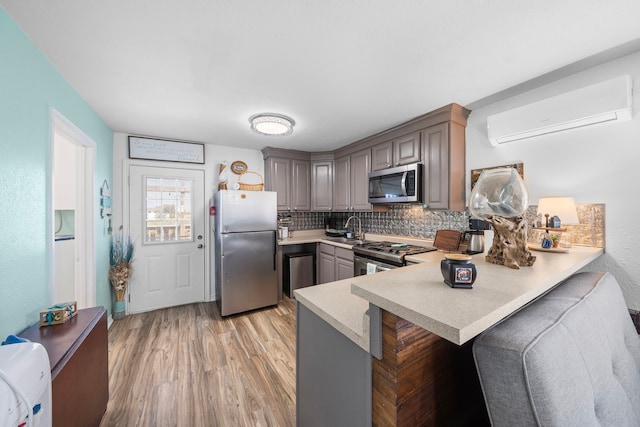 kitchen featuring appliances with stainless steel finishes, a wall mounted air conditioner, a peninsula, light countertops, and a sink