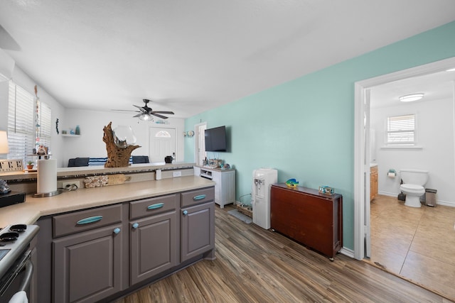 kitchen with gray cabinetry, stove, wood finished floors, a ceiling fan, and light countertops