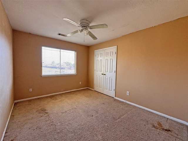 carpeted spare room featuring a ceiling fan, visible vents, and baseboards