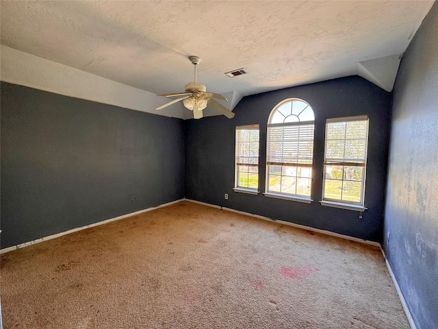 carpeted empty room featuring ceiling fan, a textured ceiling, visible vents, baseboards, and vaulted ceiling