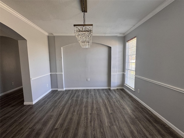 spare room featuring arched walkways, ornamental molding, dark wood-style flooring, and baseboards