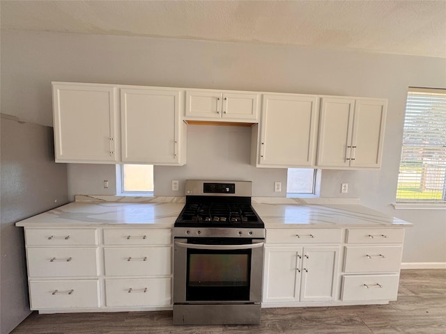 kitchen featuring stainless steel range with gas cooktop, light stone counters, white cabinets, and wood finished floors