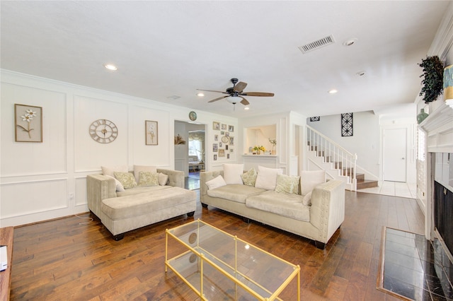 living room with dark wood-style flooring, visible vents, a decorative wall, a fireplace with flush hearth, and stairs