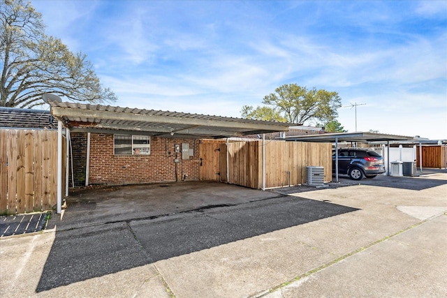 exterior space with central AC unit, brick siding, covered parking, and fence