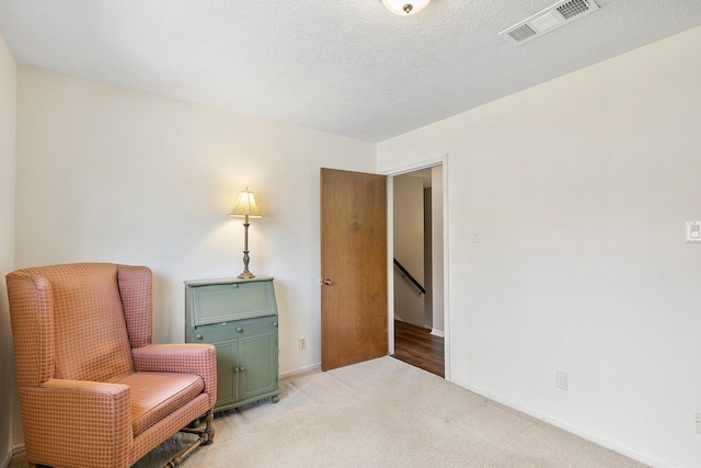 sitting room featuring visible vents, an upstairs landing, a textured ceiling, baseboards, and light colored carpet