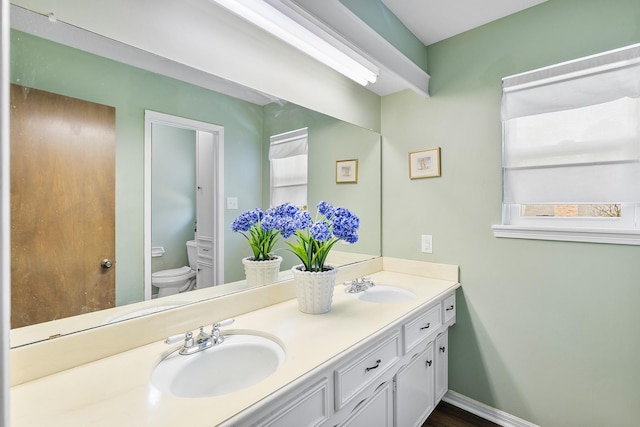 full bathroom featuring double vanity, toilet, baseboards, and a sink