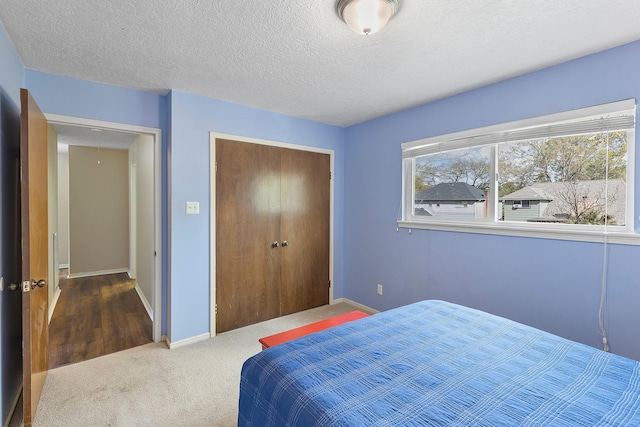 bedroom with a textured ceiling, carpet, a closet, and baseboards