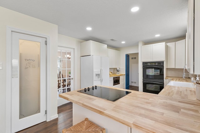 kitchen with visible vents, a sink, black appliances, white cabinets, and butcher block counters