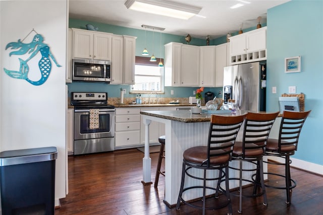 kitchen with dark wood finished floors, appliances with stainless steel finishes, white cabinets, a sink, and a kitchen bar