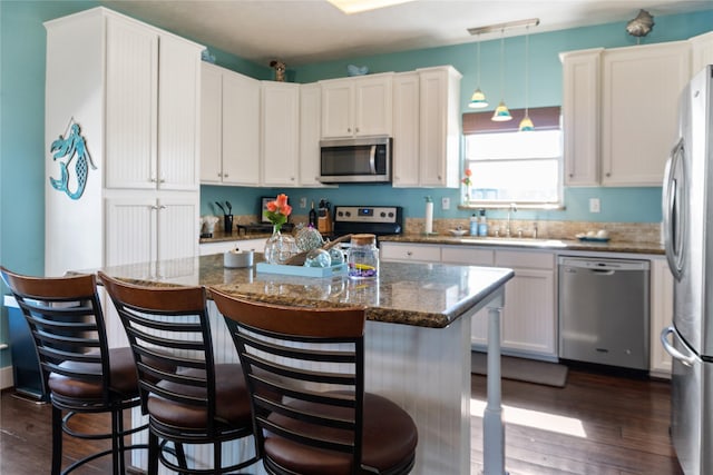 kitchen with appliances with stainless steel finishes, dark wood-type flooring, white cabinets, a sink, and dark stone countertops