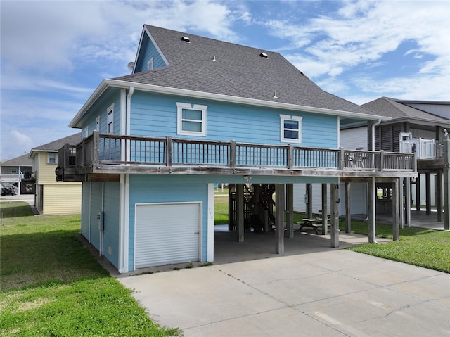 rear view of house with concrete driveway, a lawn, roof with shingles, a wooden deck, and a carport