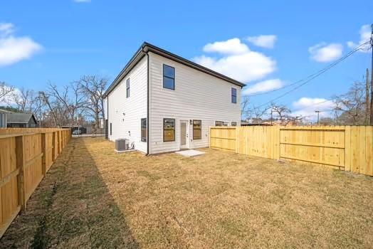 rear view of property featuring cooling unit, a fenced backyard, and a yard