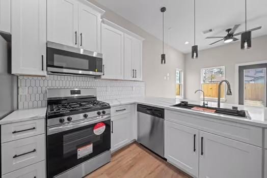 kitchen featuring stainless steel appliances, a sink, white cabinetry, light wood-type flooring, and decorative backsplash