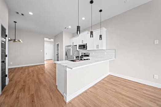 kitchen featuring white cabinets, appliances with stainless steel finishes, a peninsula, light wood-type flooring, and backsplash