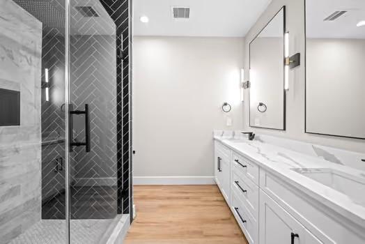 full bathroom featuring double vanity, tiled shower, baseboards, and wood finished floors