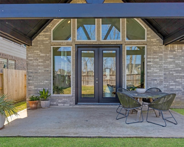 view of exterior entry featuring brick siding, a patio, french doors, and fence