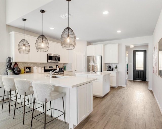 kitchen featuring visible vents, a peninsula, light wood-style flooring, stainless steel appliances, and decorative backsplash