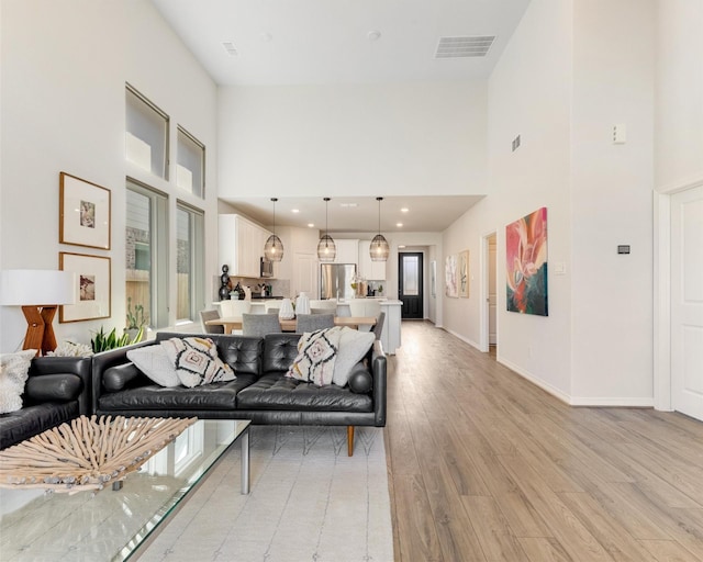 living room with visible vents, baseboards, recessed lighting, a high ceiling, and light wood-style floors