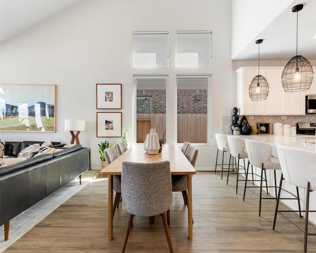 dining room with baseboards, light wood finished floors, and high vaulted ceiling