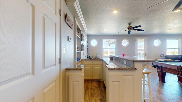 kitchen with a textured ceiling, a peninsula, wood finished floors, open floor plan, and a kitchen bar