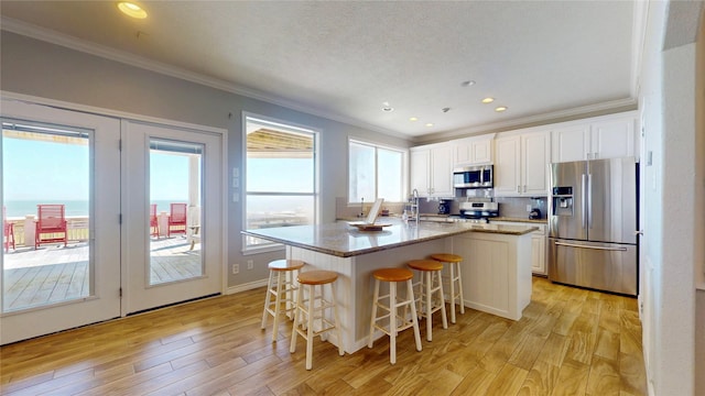 kitchen with a center island with sink, a breakfast bar area, stainless steel appliances, light wood-style floors, and white cabinets