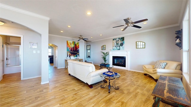 living room featuring light wood-style floors, arched walkways, a glass covered fireplace, and ornamental molding