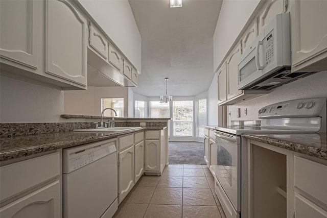 kitchen with a chandelier, a peninsula, white appliances, a sink, and dark stone countertops