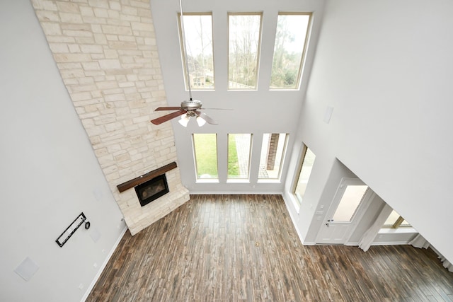 unfurnished living room with a fireplace, wood finished floors, a ceiling fan, a towering ceiling, and baseboards