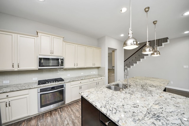 kitchen with stainless steel appliances, a sink, tasteful backsplash, dark wood finished floors, and decorative light fixtures