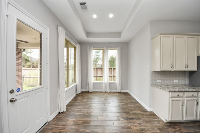 entryway with a tray ceiling, visible vents, dark wood finished floors, and baseboards