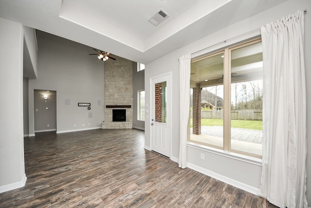 unfurnished living room with a fireplace, visible vents, dark wood-style flooring, and a ceiling fan