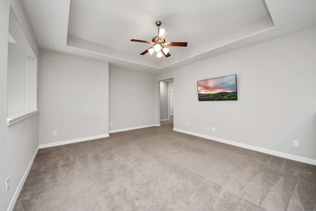 spare room featuring carpet floors, a tray ceiling, a ceiling fan, and baseboards