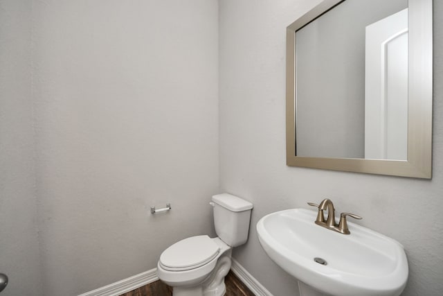 bathroom featuring toilet, baseboards, a sink, and wood finished floors