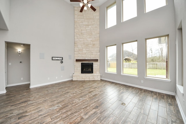 unfurnished living room featuring dark wood-style floors, ceiling fan, a fireplace, and baseboards